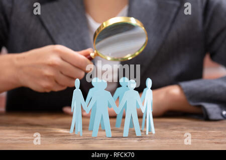 Close-up Of Businesswoman Holding Magnifying Glass Over The Human Figures Forming Circle Stock Photo