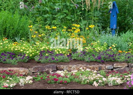 63821-21817 Flower garden with stone wall and blue bird house. raspberry blast petunia and diamond frost euphorbia in blue pot, Butterfly Bushes, Peac Stock Photo
