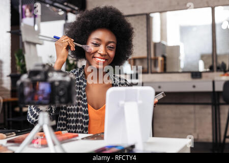 Positive dark-skinned woman with curly hair smiling brightly Stock Photo