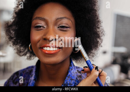 Pretty smiling dark-skinned model in an orange top looking amused Stock Photo