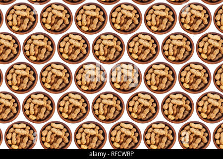 Unpeeled peanuts in a wooden cedar plate on a white isolated background. Row of bowls with peanuts, top view.  Unpeeled peanuts pattern Stock Photo