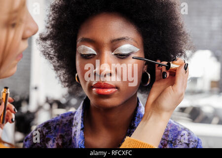 Fair-haired young stylist with black nail polish doing makeup to a model Stock Photo