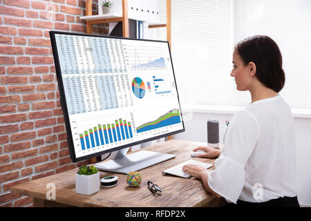 Close-up Of A Businesswoman Analyzing Graph On Computer Over The Wooden Desk In The Office Stock Photo
