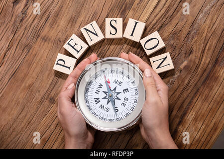 Close-up Of A Hand Holding Magnetic Compass In Front Of Pension Blocks Over The Desk Stock Photo