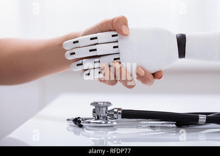 Close-up Of Female Shaking Hand With Robot Over The White Desk With Stethoscope Stock Photo