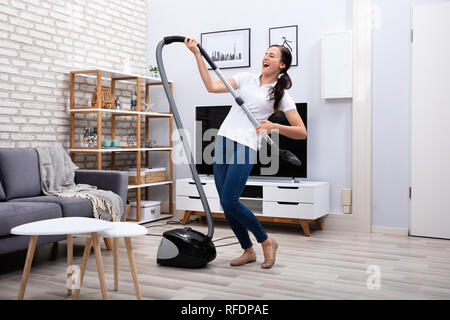 Happy Female Janitor Dancing With Vacuum Cleaner At Home Stock Photo