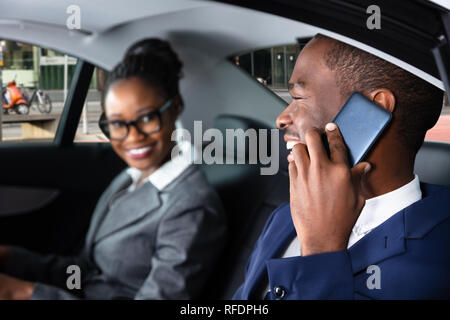 Happy Businessman Sitting Inside Car Beside His Female Colleague Talking On Cellphone Stock Photo