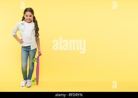 Her favorite activity. Kid girl happy holds penny board. Child likes skateboarding with penny board. Modern teen hobby. How to ride skateboard. Girl happy face holds penny board yellow background. Stock Photo