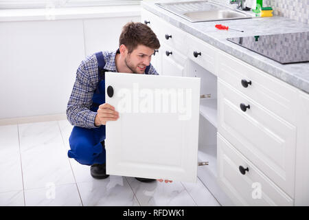 Smiling Handyman Fitting A New Door Under The Kitchen Worktop Stock Photo