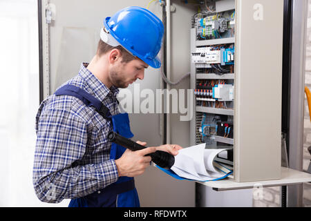 Close-up Of Male Technician Holding Flashlight And Folder File In Front Of Fuse Box Stock Photo