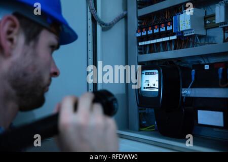 Close-up Of A Electrician Examining A Fuse Box With A Torch Stock Photo
