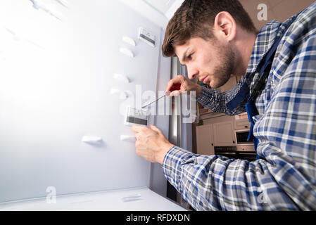 Male Worker Repairing Refrigerator With Hand Tool In Kitchen Room Stock Photo