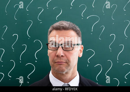 Thinking Mature Man In Front Of Question Marks Drawn On Chalkboard Stock Photo