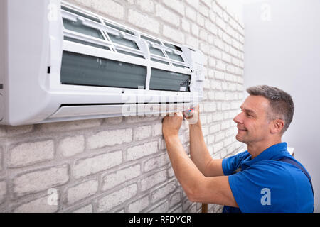 Mature Male Technician Fixing Air Conditioner With Screwdriver Stock Photo