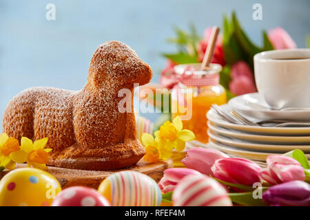 Easter tea table with a speciality lamb cake, decorated Easter eggs and fresh spring flowers with yellow daffodils and colorful tulips Stock Photo