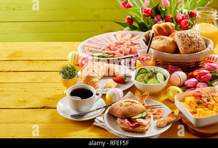 Easter buffet breakfast or brunch with assorted bread rolls, cheese, meat, scrambled egg, orange juice, coffee on a wooden table decorated with easter Stock Photo