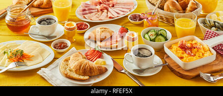 Easter breakfast panorama banner with a wholesome spread of assorted bread rolls, croissant, cheese, cold meats, orange juice, coffee, honey and prese Stock Photo