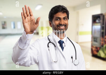 Indian medic or physician waving hand with cheerful expression as greeting someone in the hospital corridor Stock Photo