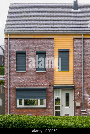 modern dutch terrace house decorated with plants behind the windows, some windows closed down with roller shutters, home in a dutch small village Stock Photo