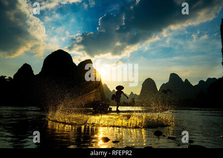 Silhouette of Cormorant fisherman using net on the ancient bamboo boat Stock Photo