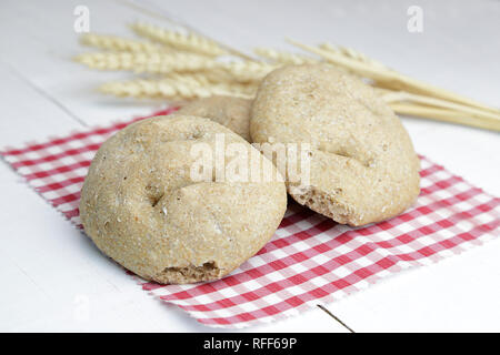 Three pieces of brown bread and a branch of wheat over a red and white checkered napkin on a white wooden table Stock Photo