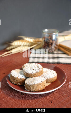 In the foreground a plate with some cinnamon shortbread in the background, out of focus, on a tablecloth, some ingredients like cinnamon, coffee and w Stock Photo