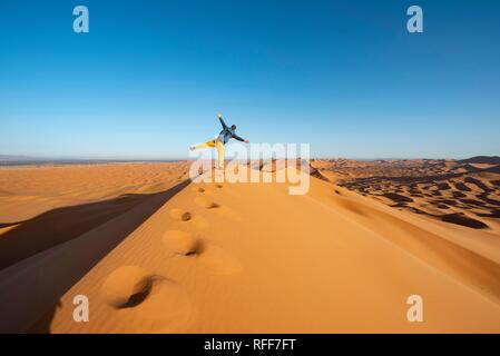Young man on sand dune standing on one leg, Erg Chebbi, Merzouga, Sahara, Morocco Stock Photo