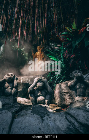 Statue at the Golden Mountain in Bangkok. 3 Monkeys in the foreground and in the back golden Statue between fog and the garden.  Stock Photo