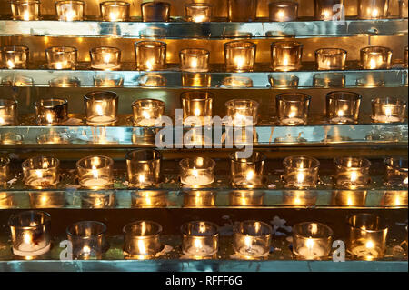 Many candles lined up in Holy Rosary Cathedral in Vancouver, Canada, shining golden in front of a silver background Stock Photo