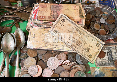 Very old Philippine bank notes and coins mixed with antique spoons on a table in a wet market in the city of Iloilo, Philippines Stock Photo