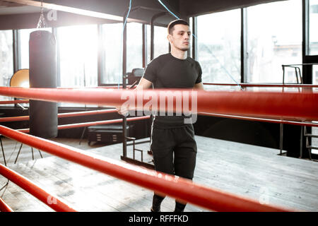 Young athletic man in black uniform training with a jumping rope, warming up on the boxing ring in the gym Stock Photo