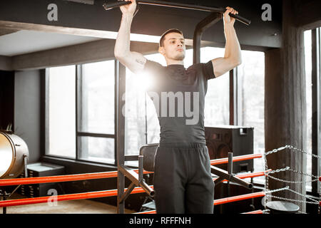 Young athletic man pulling up on the bar, warming up before the training on the boxing ring at the gym Stock Photo