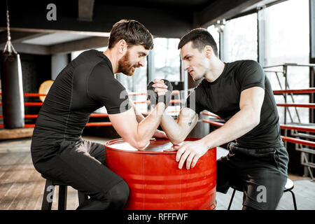 Two young athletes in black sportswear having a hard arm wrestling competition on a red barrel in the gym Stock Photo