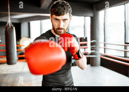 Portrait of an athletic man as a boxer in red boxing gloves on the fighting ring at the gym Stock Photo