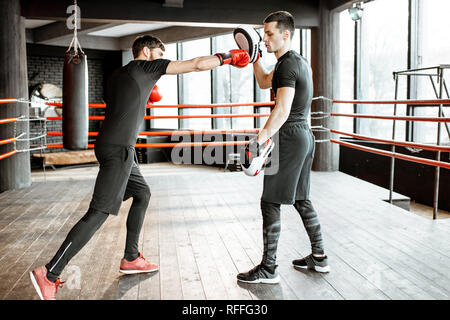 Boxing trainer showing to a man how to fight, teaching to box on the boxing ring at the gym Stock Photo