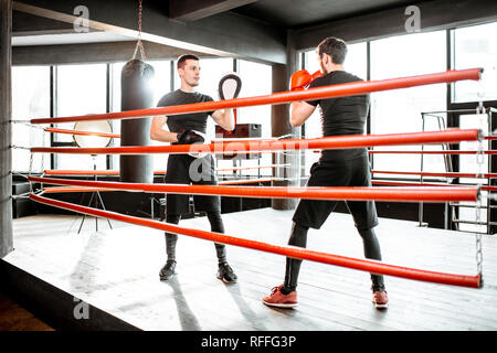 Athletic man fighting during the training with boxing trainer on the boxing ring at the gym Stock Photo