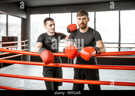 Portrait of a two athletic men in black sportswear during the break on the boxing ring at the gym Stock Photo