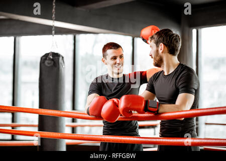 Two athletic men in black sportswear talking together, having fun during the break on the boxing ring at the gym Stock Photo
