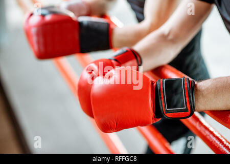 Boxers resting on the boxing ring, close-up view on the boxing gloves on the ropes Stock Photo