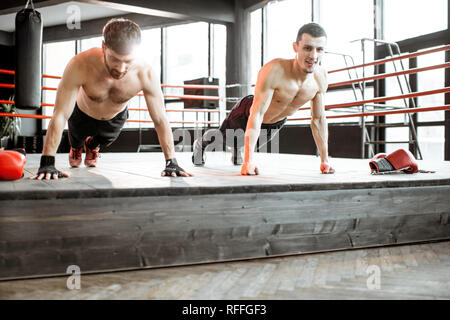 Two athletic men doing push-ups on the boxing ring, training before boxing at the gym Stock Photo