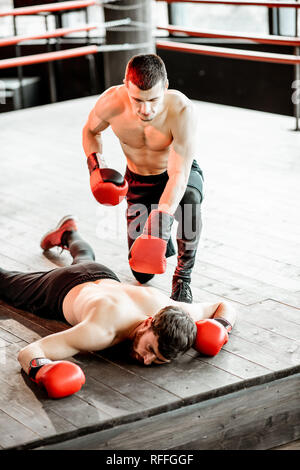 Beaten boxer lying knocked out on the boxing ring with strong man winner above Stock Photo