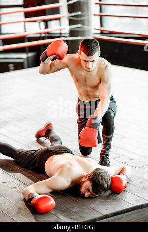 Beaten boxer lying knocked out on the boxing ring with strong man winner above Stock Photo