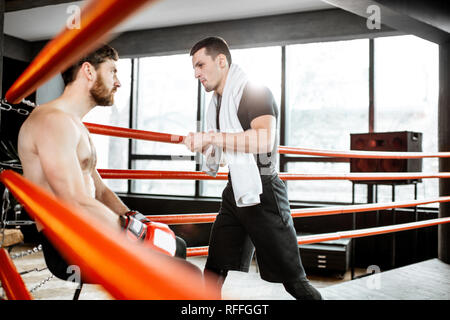 Boxing trainer giving instructions during a break motivating a boxer sitting on the corner of the boxing ring Stock Photo