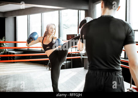 Young woman training to box with personal coach on the boxing ring at the gym Stock Photo
