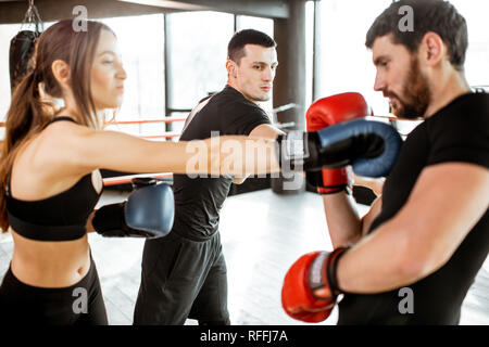 Man and woman training to box with personal coach on the boxing ring at the gym Stock Photo