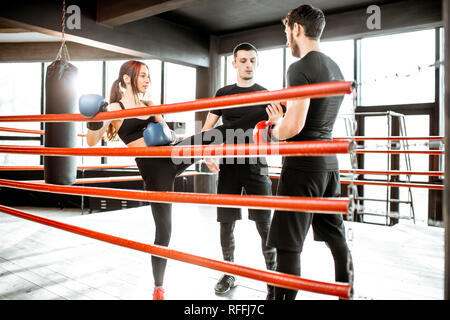 Man and woman training to box with personal coach on the boxing ring at the gym Stock Photo