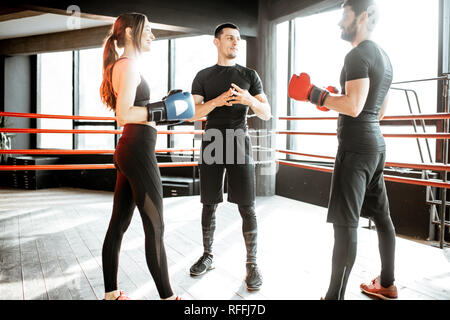 Man and woman training to box with personal coach on the boxing ring at the gym Stock Photo