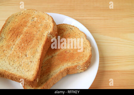 Two pieces of toasted whole wheat multigrain sliced bread on white plate served on wooden table Stock Photo