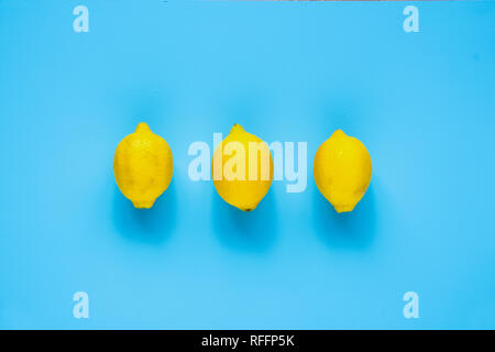 Three whole organic lemons on blue background flat lay. Top view, food composition Stock Photo