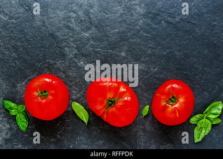 Flat-lay of tomato and basil leaves on dark copy space background top view Stock Photo